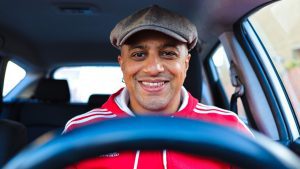 Man smiling and looking into camera while driving a vehichle.