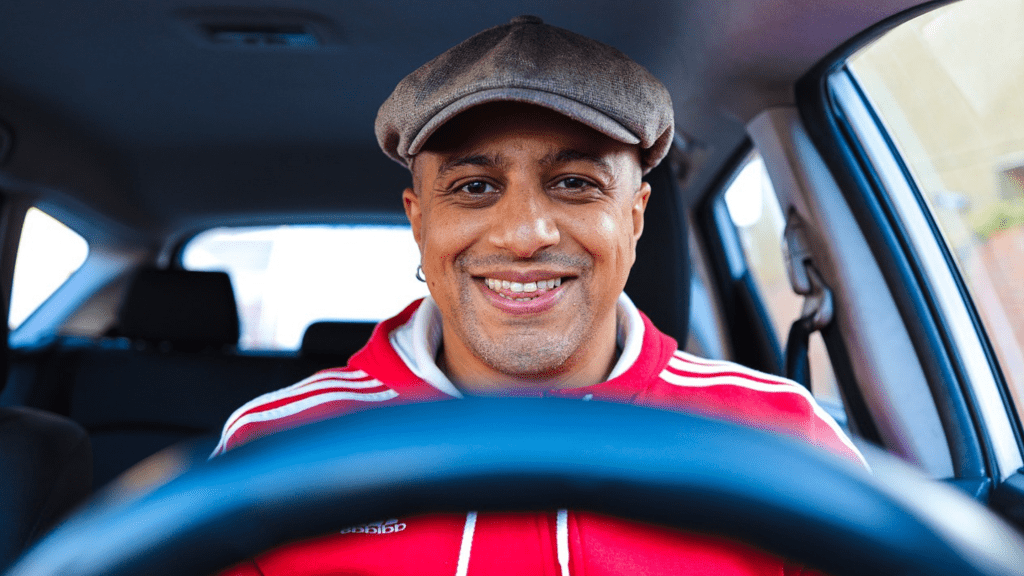 Male driver smiling and behind steering wheel.