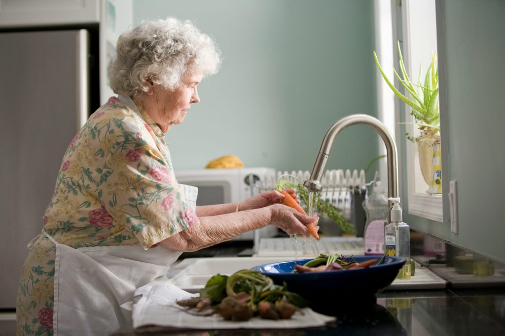 Senior woman at the sink washing vegetables